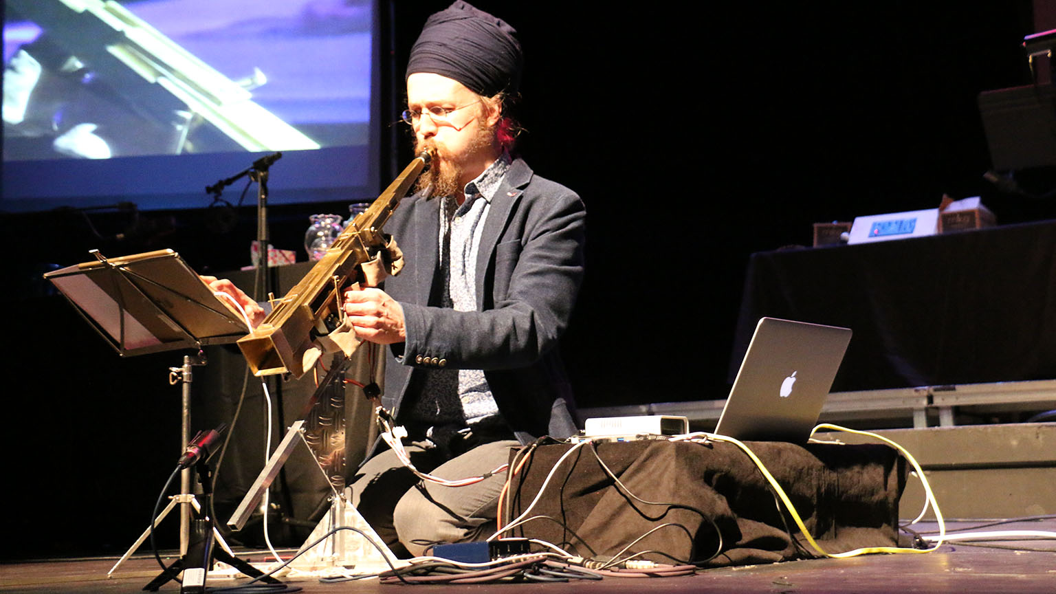 A man playing a custom made instrument sitting on stage.